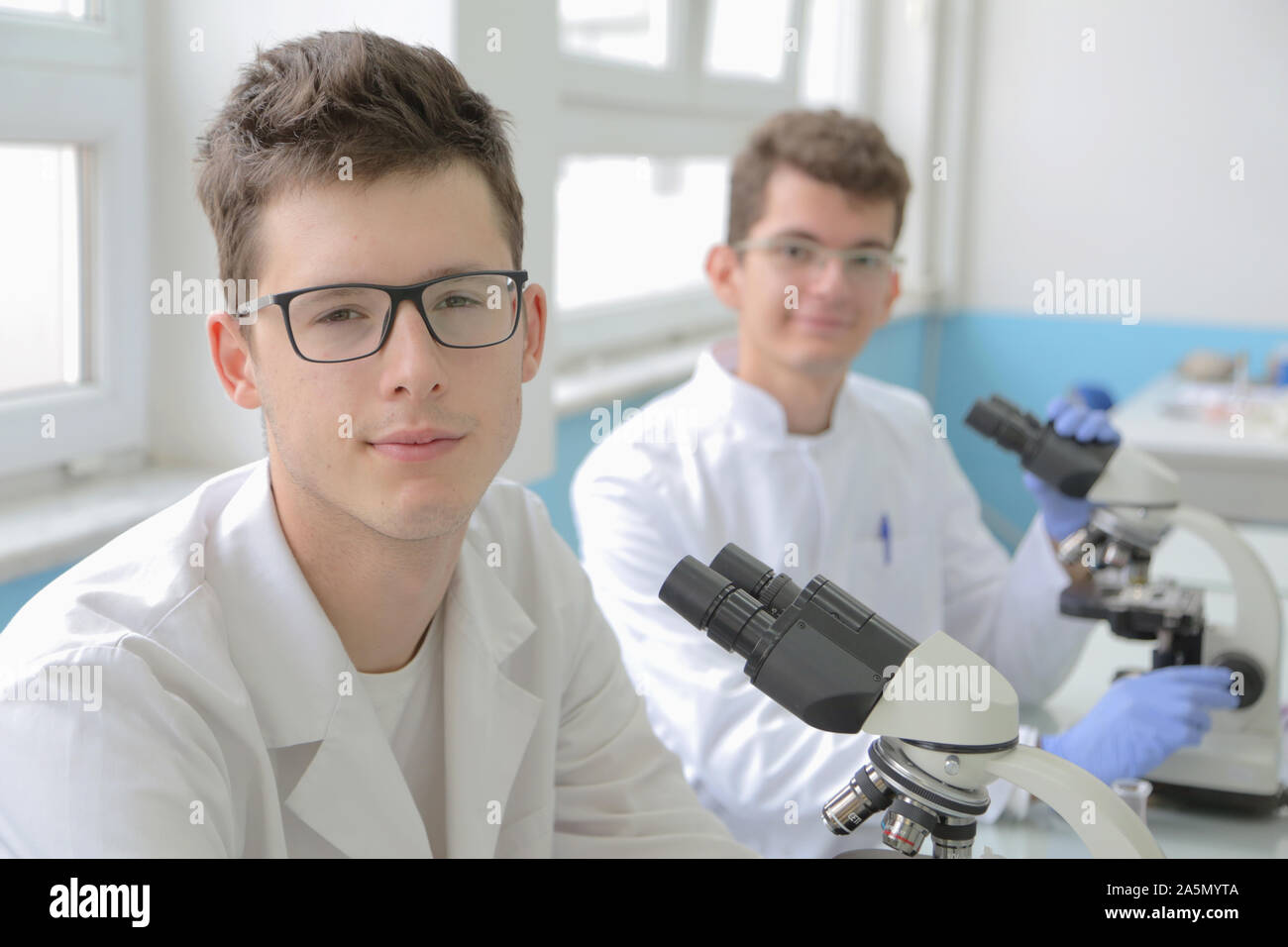 Two Young male scientists looking through a microscope in a laboratory ...