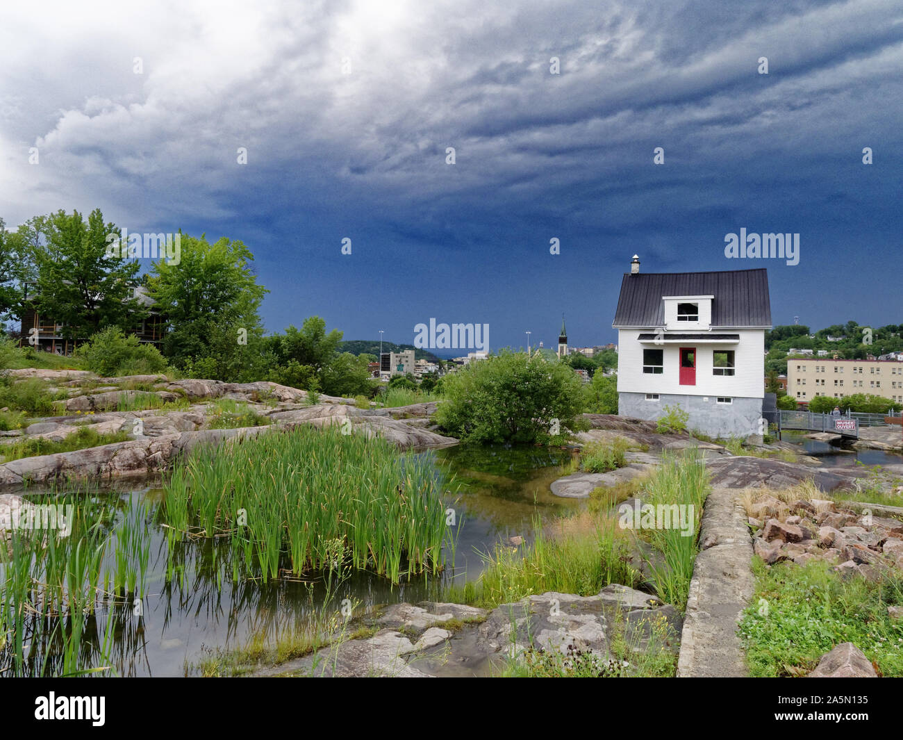 The famous little white house (La Petite Maison Blanche) in Saguenay that withstood the 1996 flooding, with stormy skies beyond Stock Photo