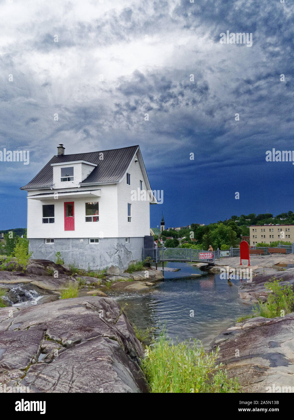 The famous little white house (La Petite Maison Blanche) in Saguenay that withstood the 1996 flooding, with stormy skies beyond Stock Photo