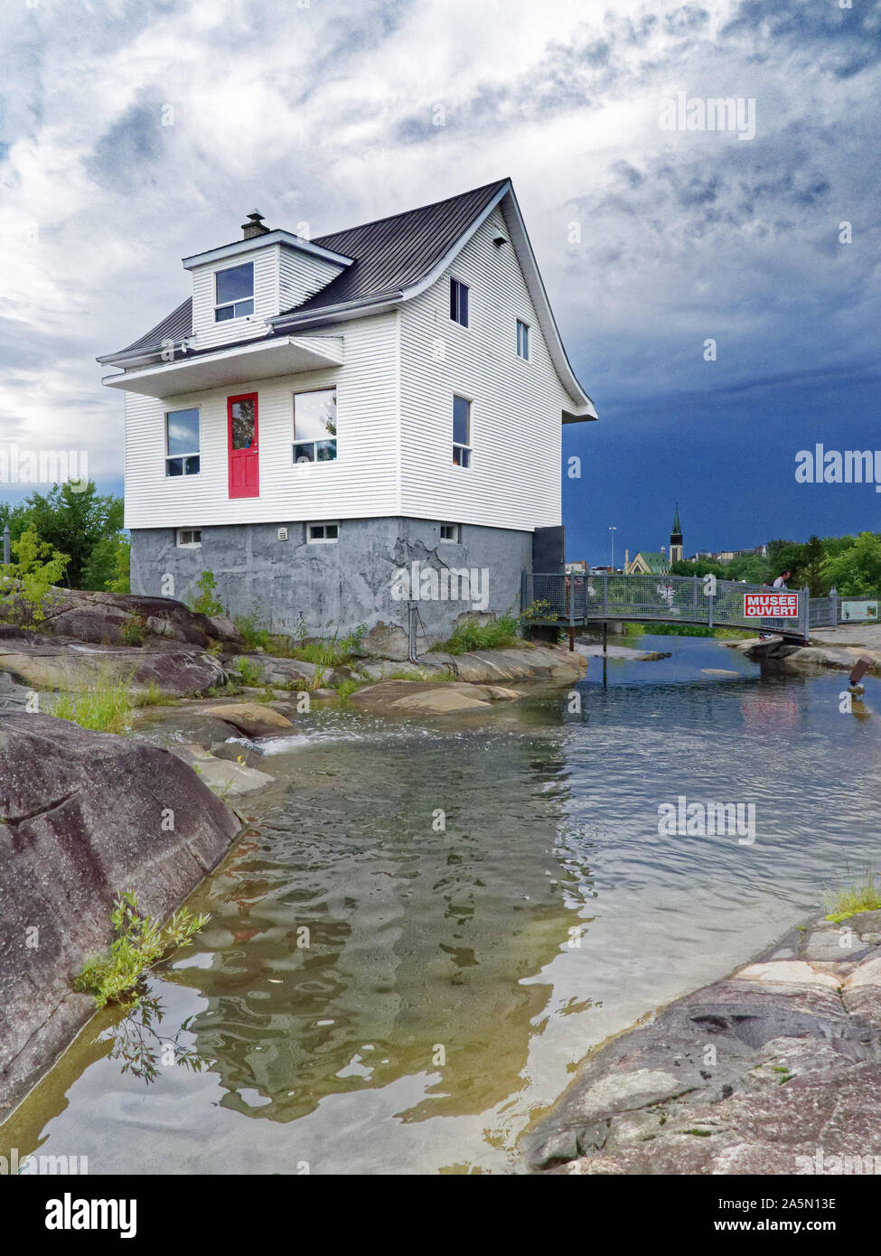 The famous little white house (La Petite Maison Blanche) in Saguenay that withstood the 1996 flooding, with stormy skies beyond Stock Photo