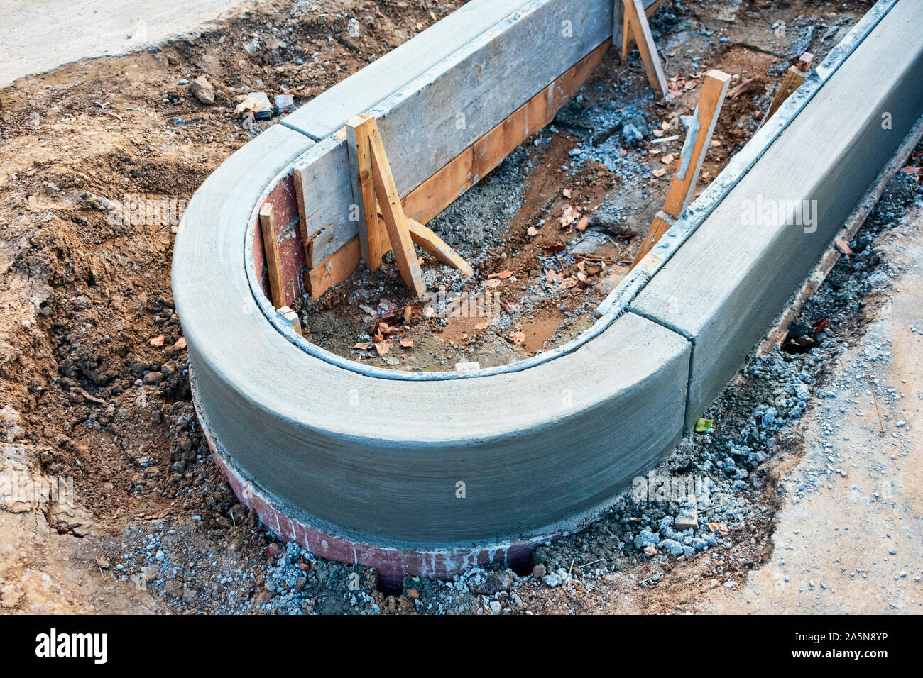 Concrete curb installation. Excavated area. Wood board secured upright with wood stakes driven