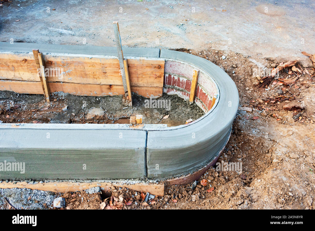 Concrete curb installation. Excavated area. Wood board secured upright with wood stakes driven