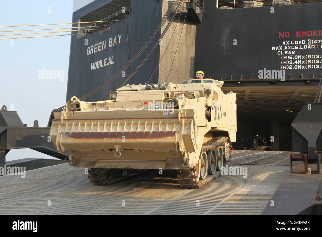 An other country another port worker drives an M9 Armored Combat Earthmover off of the Green Bay vessel at Shuaiba Port, Kuwait, Oct. 20, 2019. 1188th Deployment and Distribution Support Battalion (DDSB) Soldiers and other country national port workers conducted 24-hours of continuous operations to offload this, and other equipment belonging to the 30th Armored Brigade Combat Team (ABCT), from the vessel. The 30th ABCT will replace the 3rd ABCT, 4th Infantry Division and assume the Task Force Spartan mission in the coming weeks. (U.S. Army Reserve photo by Spc. Dakota Vanidestine) Stock Photo