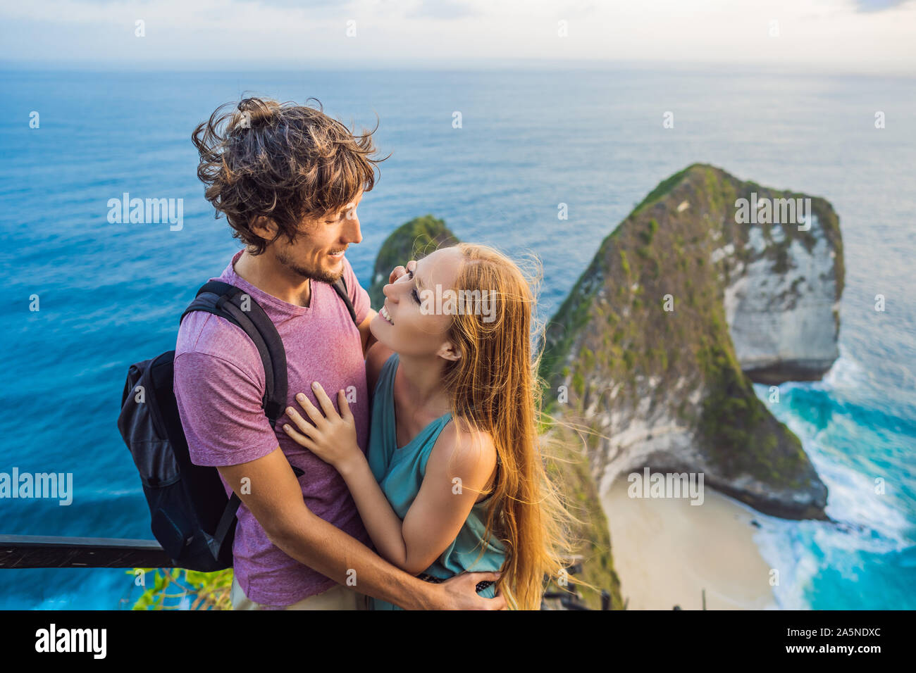 Family vacation lifestyle. Happy couple - man and woman stand at viewpoint. Look at beautiful beach under high cliff. Travel destination in Bali Stock Photo