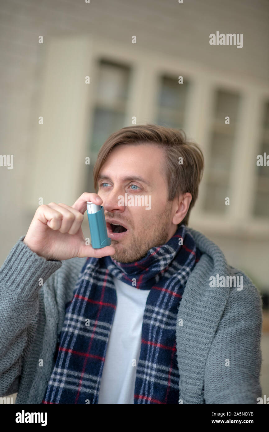 Blue-eyed young man having asthma using inhalator Stock Photo