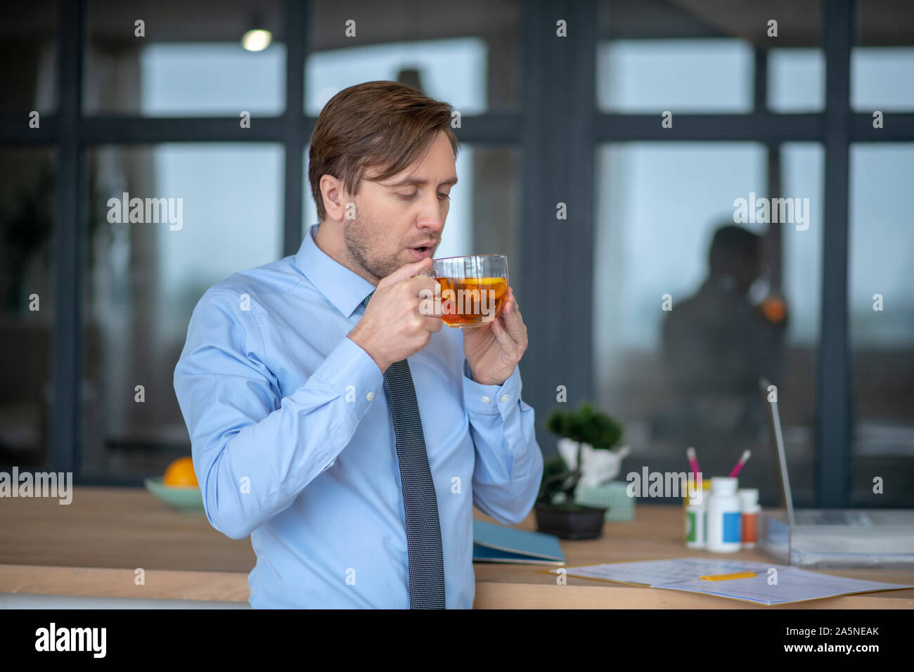 Businessman drinking hot tea while suffering from sore throat Stock