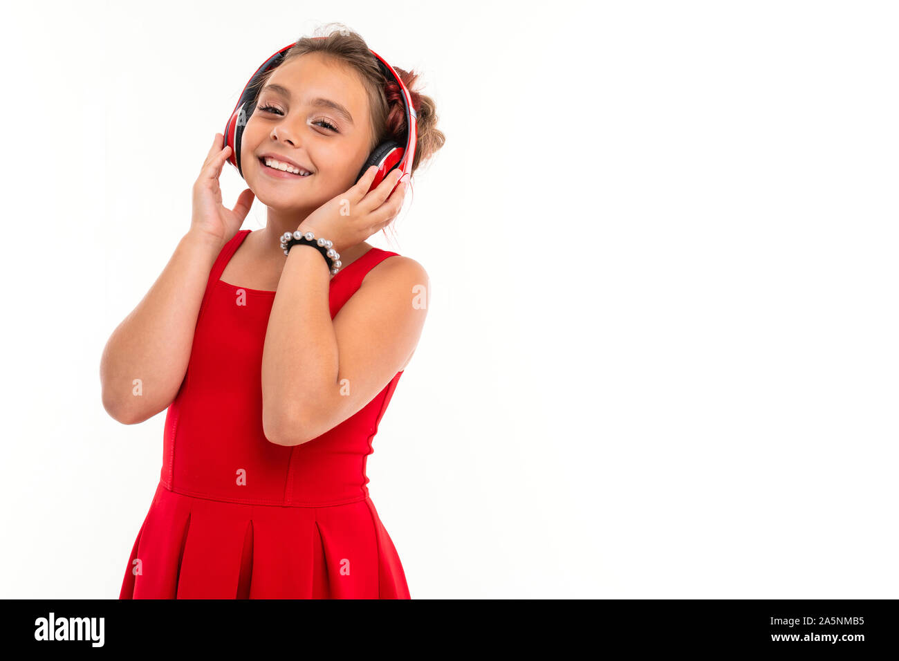 Teenage girl with long blonde hair, dyed tips pink, stuffed in two tufts, in red dress, with red headphones, bracelet, standing and listen to music Stock Photo