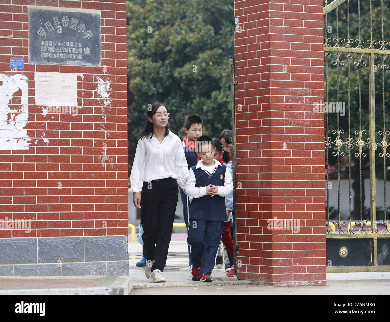 (191022) -- LUOTIAN, Oct. 22, 2019 (Xinhua) -- Fang Rong walks students home in Luotian County, central China's Hubei Province, Oct. 11, 2019. Fang Rong, 29, is the headmaster of Hope primary school of Luotian County, her alma mater. Born in a poverty-stricken region, Fang Rong was a left-behind girl. Thanks to the Hope Project and people's aids, she succeeded in graduating from a secondary normal school. To help more children and repay people's kindness, she decided to be a teacher at her alma mater. In spite of the austere way of life, Fang shouldered her responsibility from various asp Stock Photo