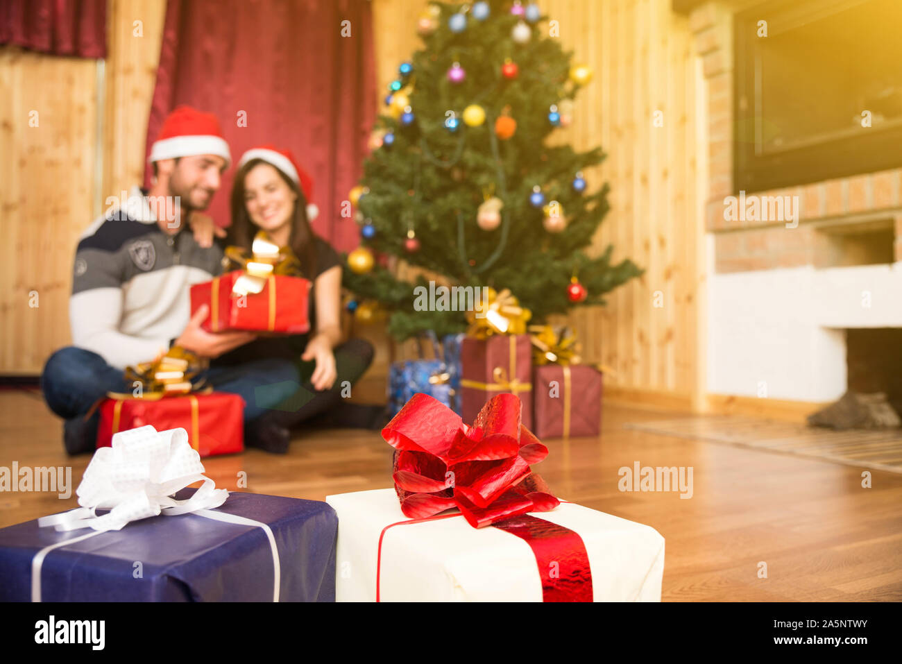 Loving couple celebrating Christmas night together sitting next to the tree holding gifts Stock Photo