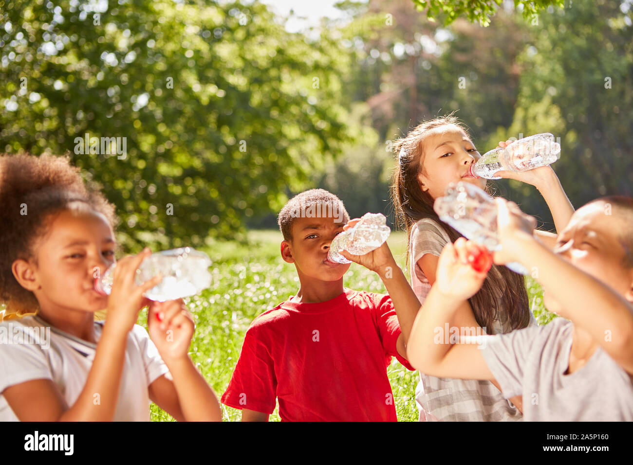 Multicultural kids drink bottled water during summer outing Stock Photo