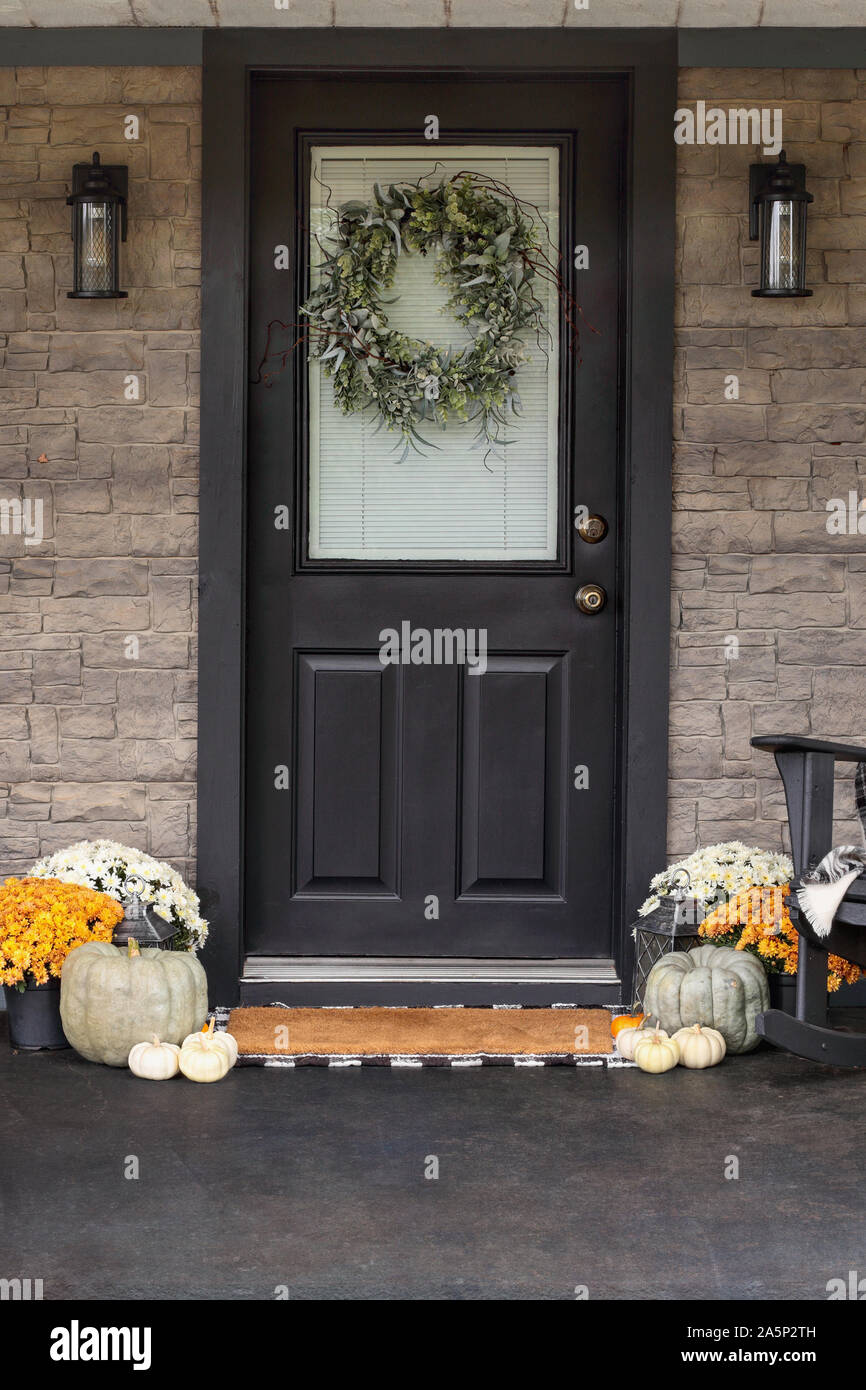 Front porch decorated for Thanksgiving Day with homemade wreath hanging on door. Heirloom gourds,  white pumpkins, and mums giving an inviting atmosph Stock Photo