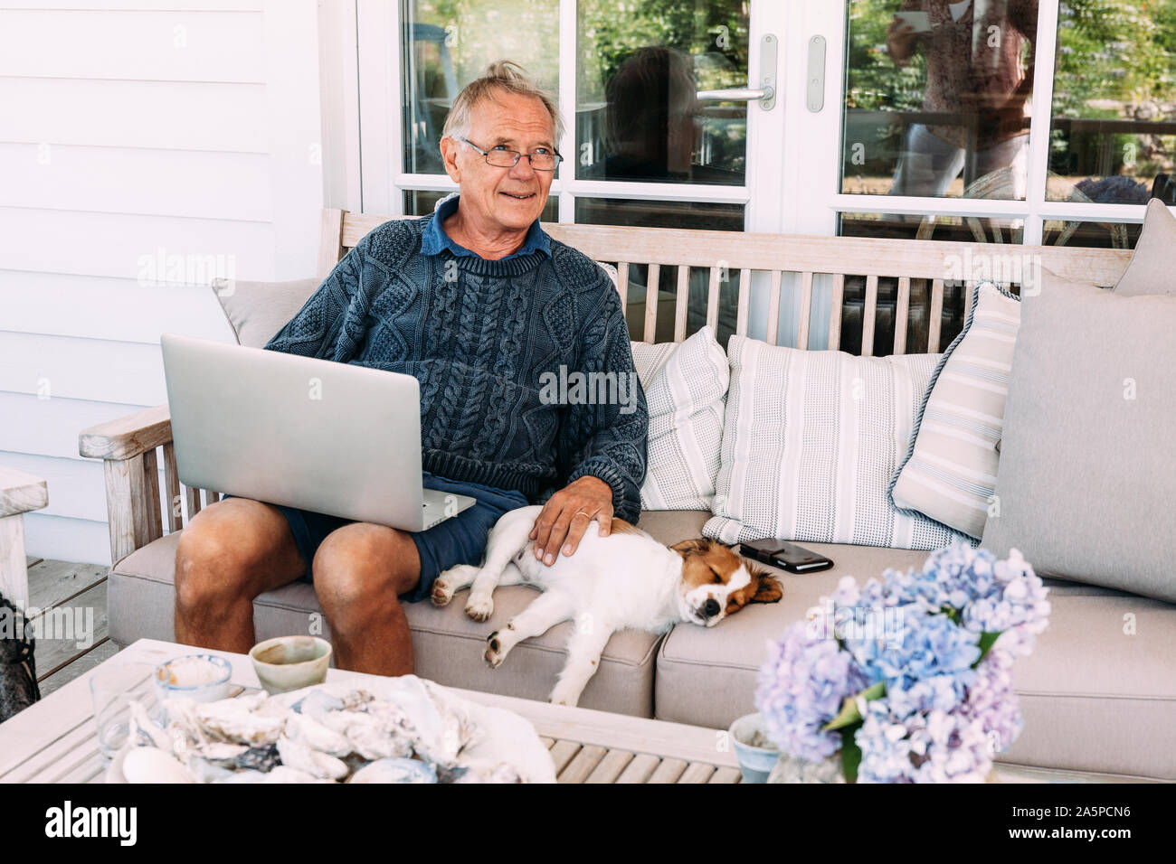 Man using laptop, sitting next to dog on sofa Stock Photo