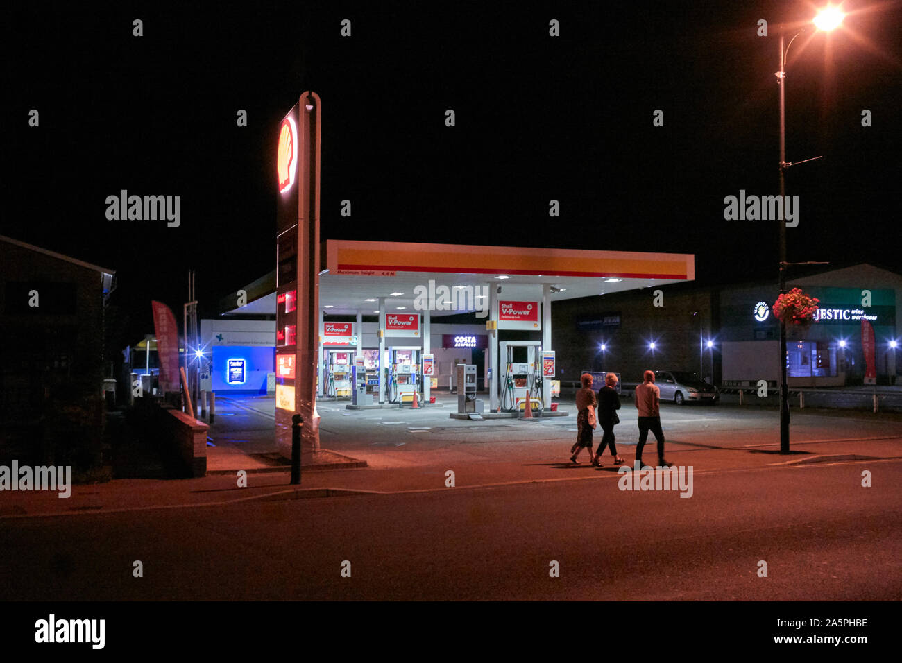 Three people walking past a Shell petrol station at night in Leighton Buzzard Stock Photo