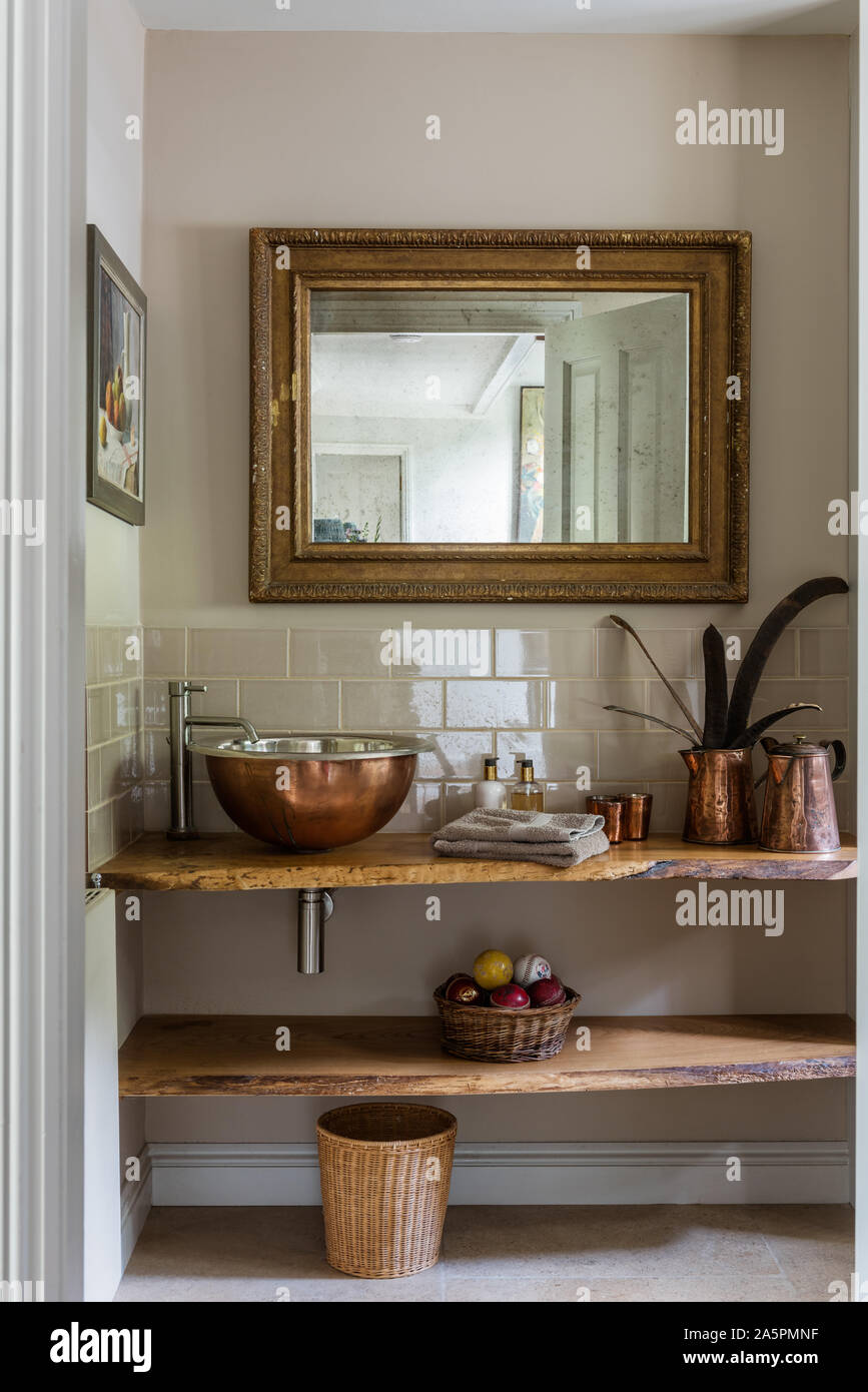 Copper sink and jugs with gilt framed mirror. shelf of natural elm made by Dominic Ash. Stock Photo
