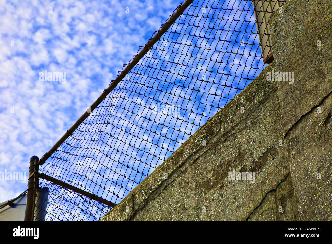 Old chain link fence on top of a wall. Stock Photo