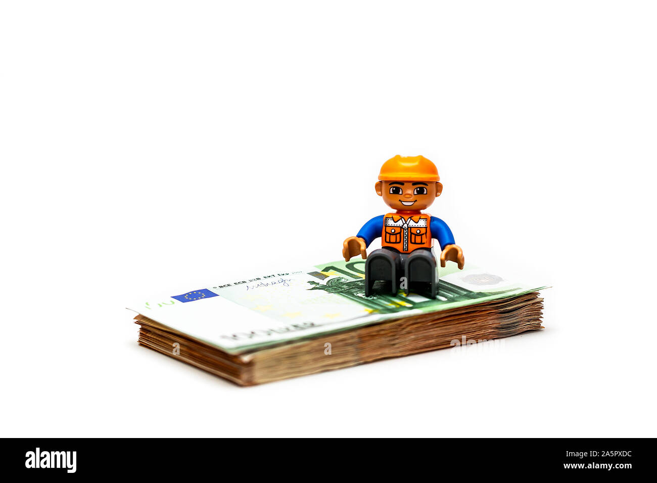 Minifigure toy worker model standing of a pilo of euro banknote, money. Lego minifigures are manufactured by the Lego Group Stock Photo