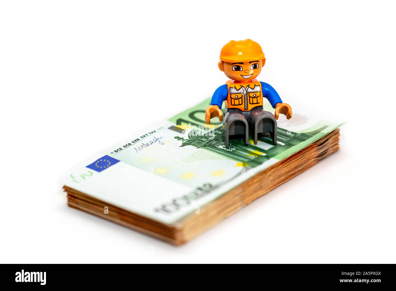 Minifigure toy worker model standing of a pilo of euro banknote, money. Lego minifigures are manufactured by the Lego Group Stock Photo