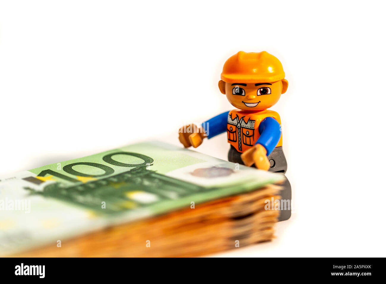 Minifigure toy worker model standing of a pilo of euro banknote, money. Lego minifigures are manufactured by the Lego Group Stock Photo