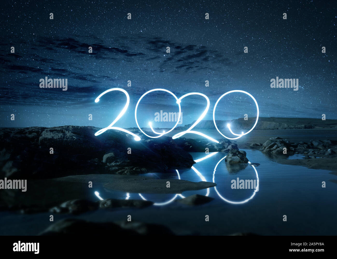Night time 2020 light effect writing reflecting in water on a beach. Long exposure Landscape new year photo composite. Stock Photo