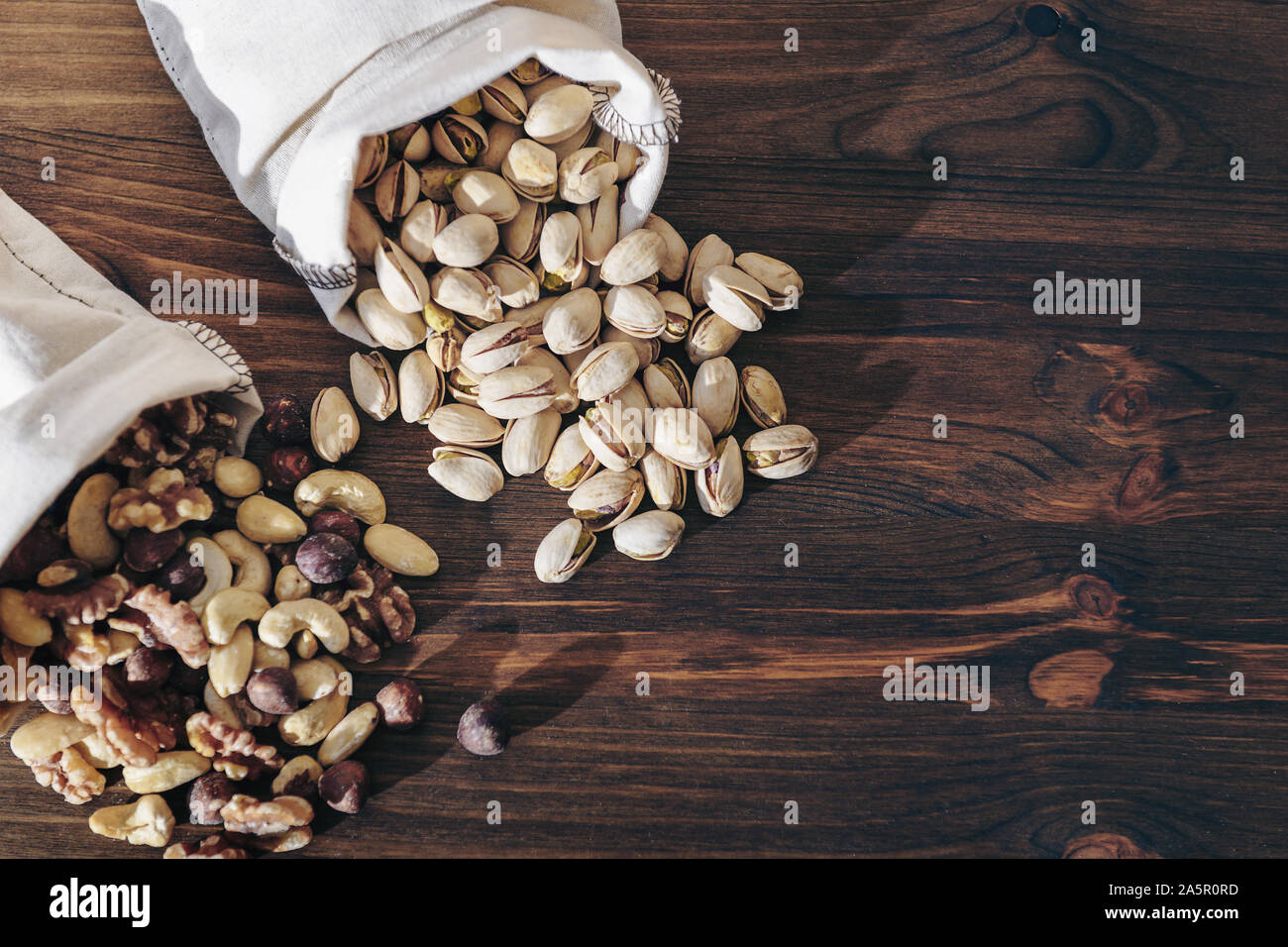 mix nuts, dry fruits and pistachios on a wooden background in hessian bags, healthy food and snack concept, copy space for text Stock Photo