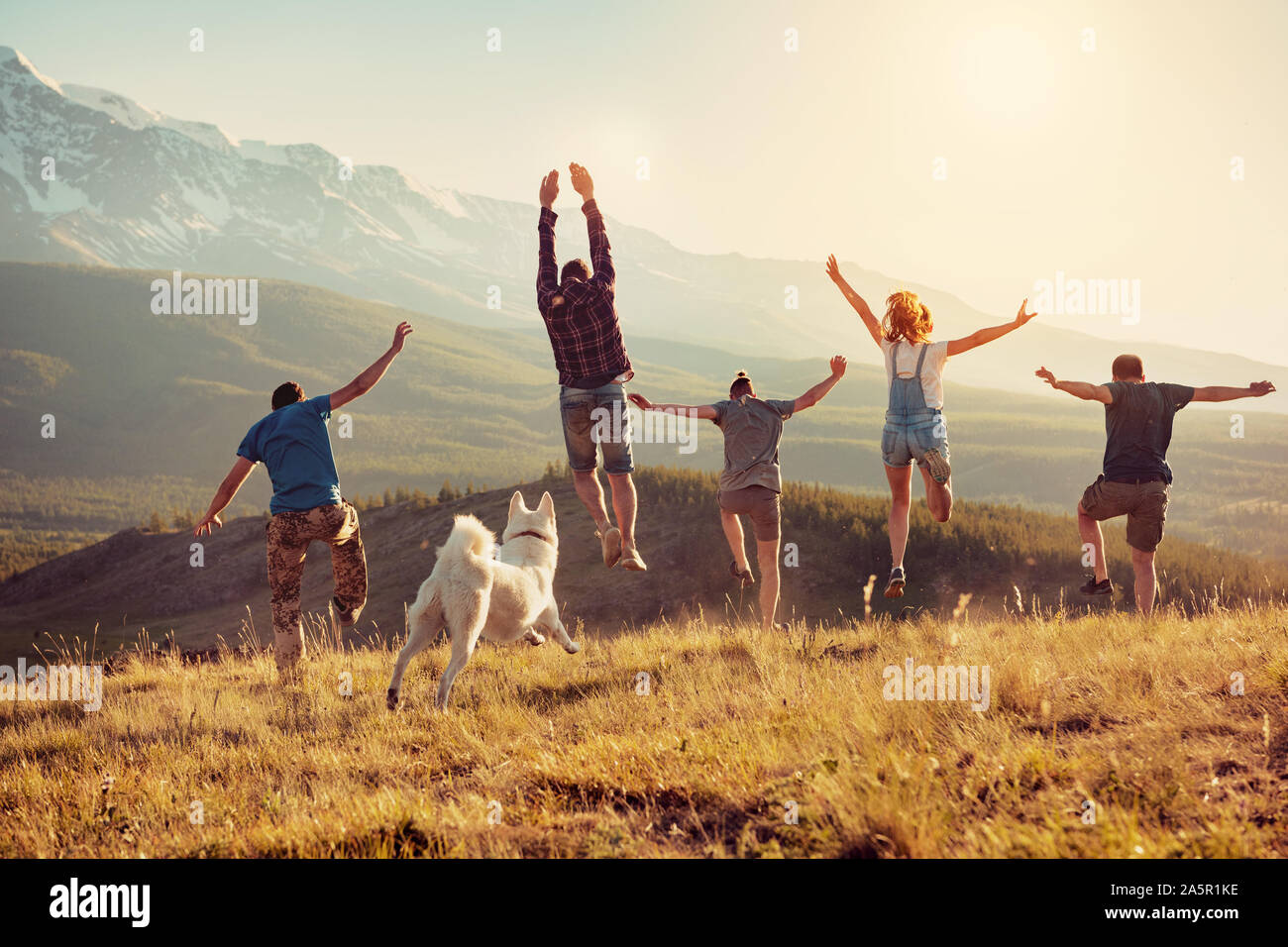 Group of happy friends are having fun, runs and jumps in mountains at sunset Stock Photo