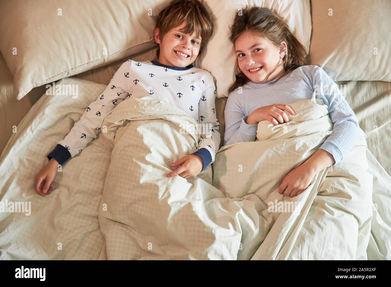 Brother and sister lie in bed and smile contentedly and happily Stock