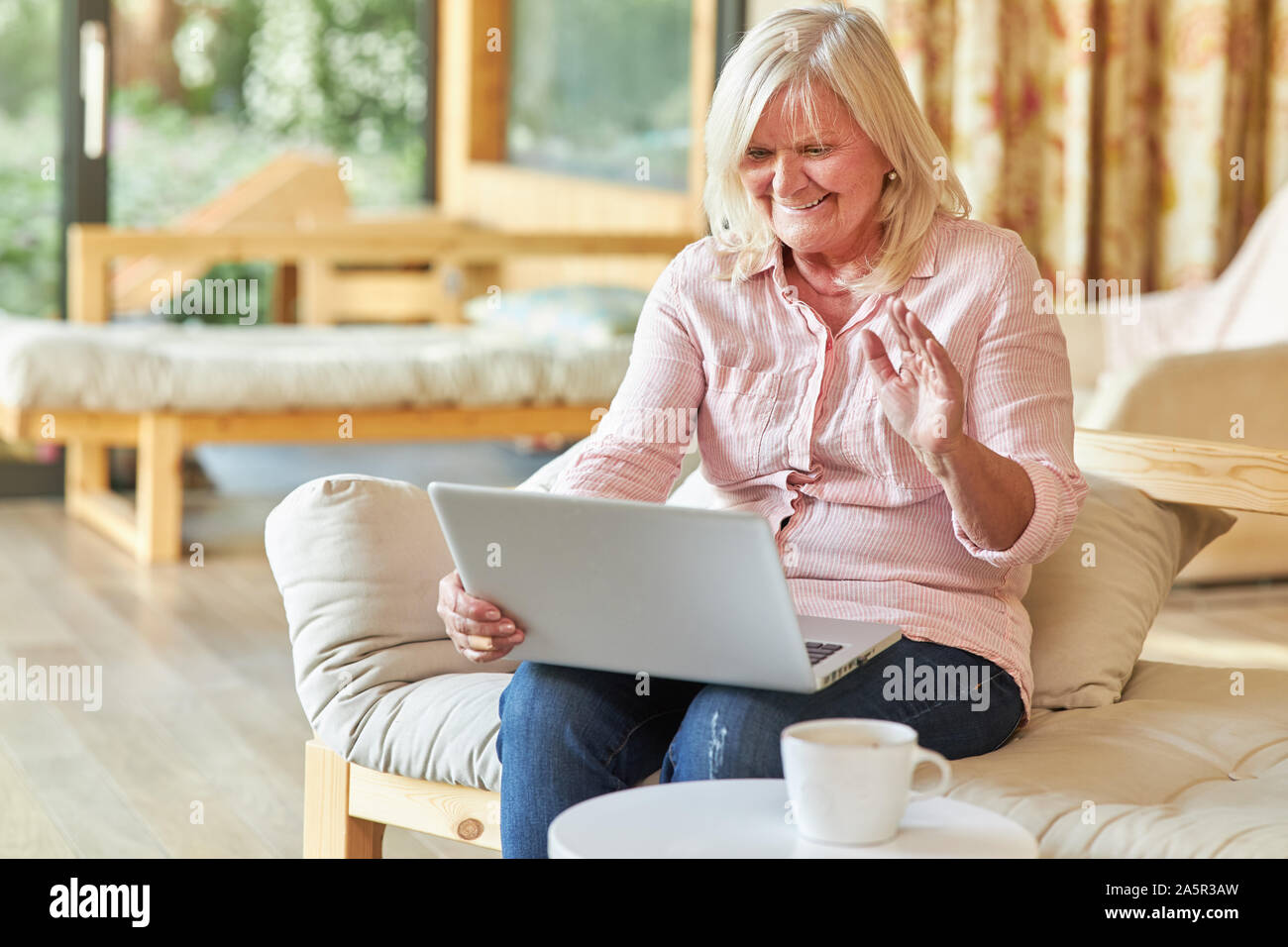 Smiling senior woman makes video chat on laptop computer in living room Stock Photo