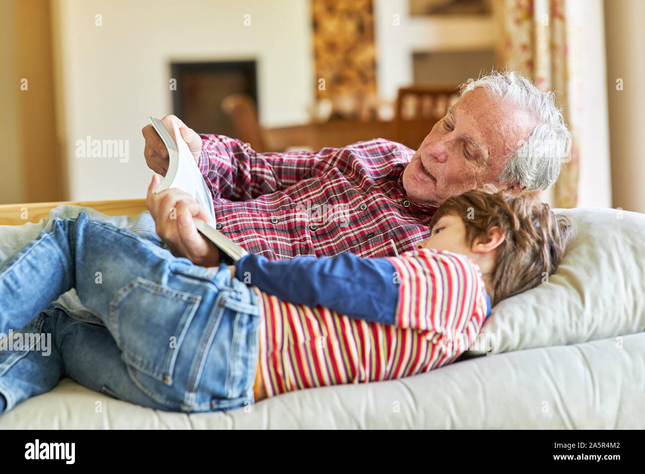 Grandpa reading a book with his grandchild on the couch at home Stock Photo