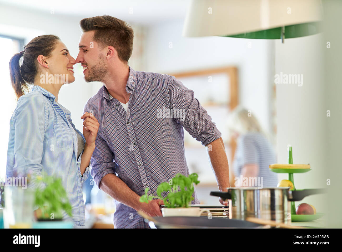 Young man kisses his girlfriend in the kitchen while cooking Stock Photo