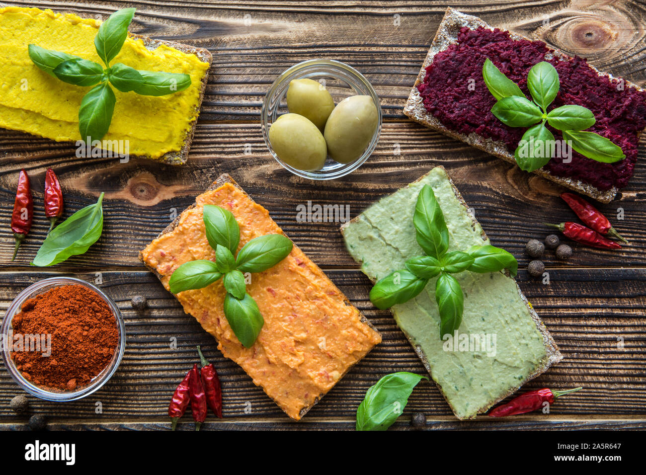 Different kinds of hummus on brown table. Sweet paprika, curry spice taste, beetroot with frsh asil eaves and avocado. Stock Photo