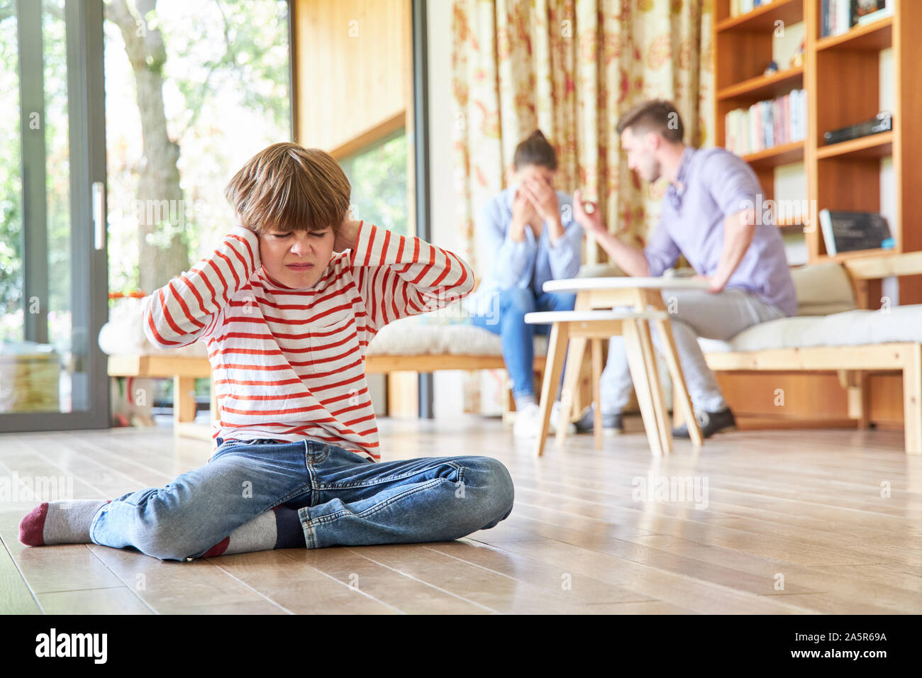 Boy covers his ears at the loud argument of the parents in the living