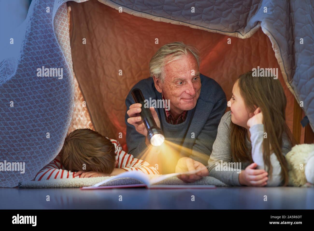 Grandpa reads grandchildren story under a blanket as a tent at home Stock Photo