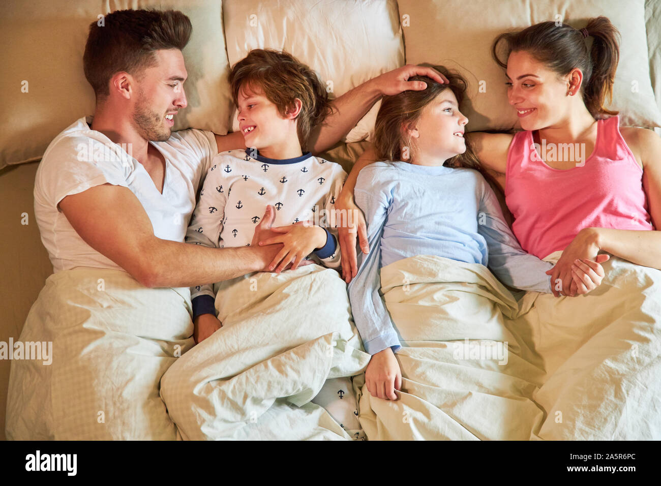 Parents and children happily cuddle together in bed in the morning in