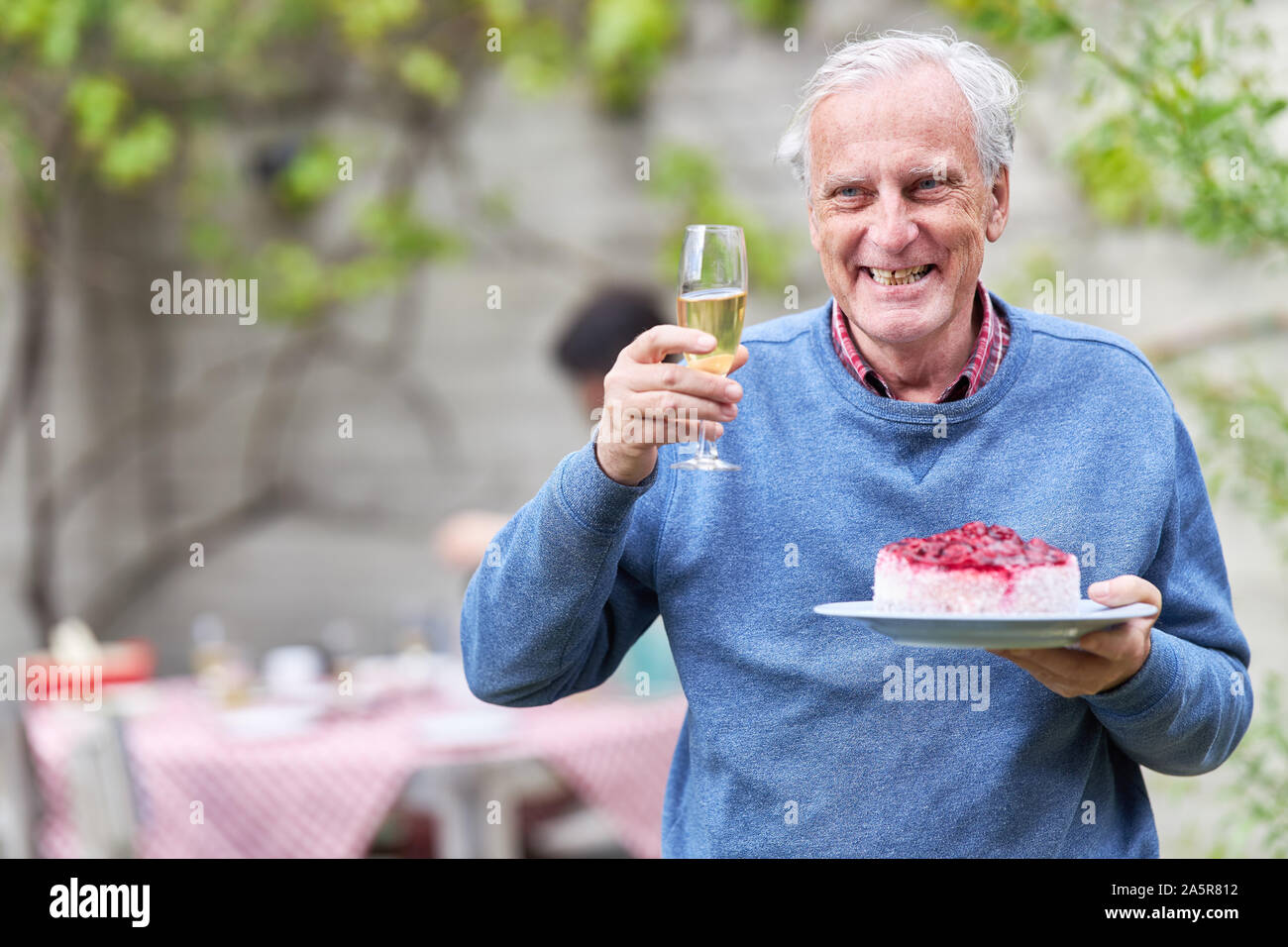 Senior man with champagne glass and a piece of birthday cake at a garden party Stock Photo