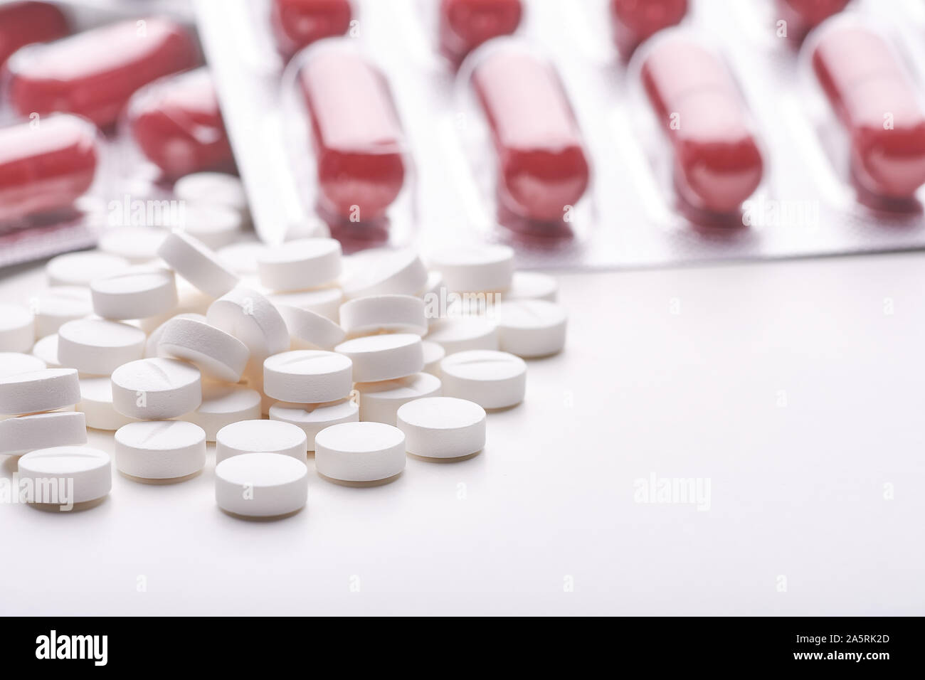 Still life with pile of round pills or tablets, antidepressants or painkillers with space for text. Red capsules in blister pack on white table top. Stock Photo
