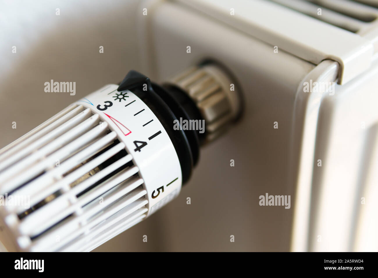 Radiator thermostat valve set to number three icon (middle position), symbol for saving money at heating costs or medium temperature setting, closeup Stock Photo