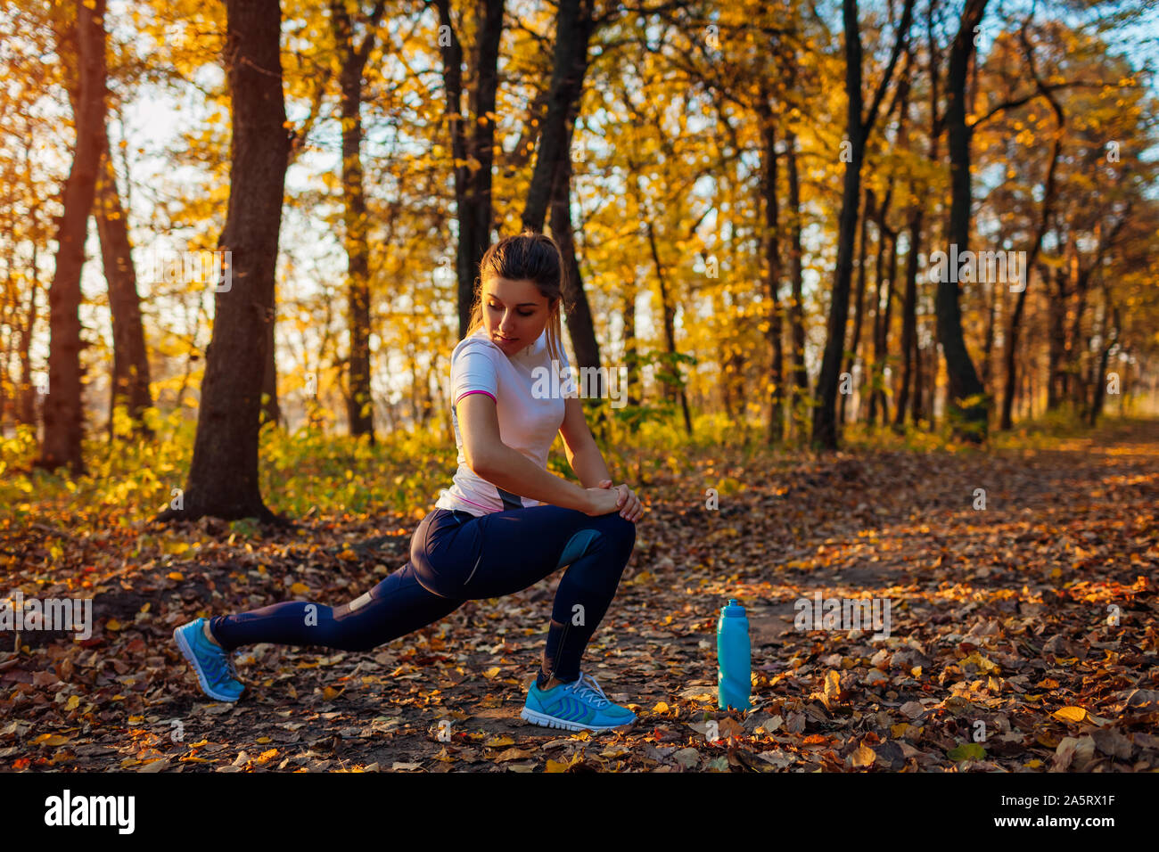 Training and exercising in autumn park. Young woman stretching legs outdoors. Active healthy lifestyle. Workout Stock Photo