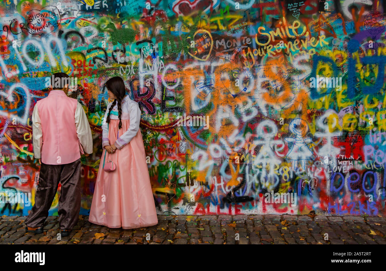 A picture of a couple dressed in traditional costume posing in front of the John Lennon Wall (Prague). Stock Photo