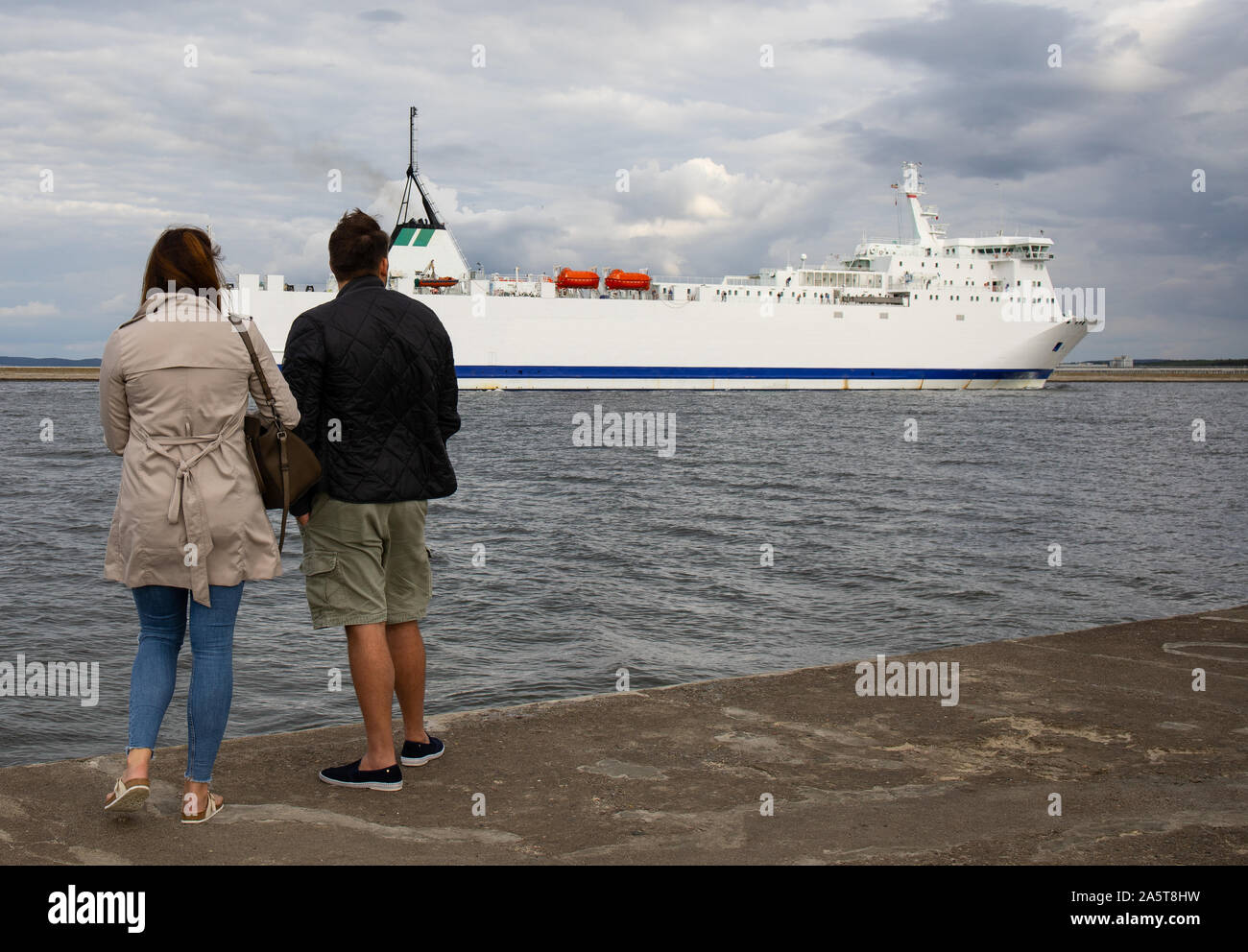 merchant ship entering the Baltic port in Poland,woman and man watch the sailing ship Stock Photo