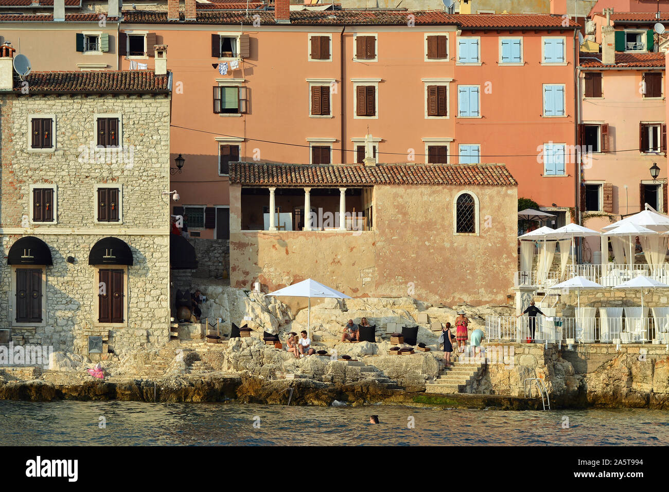 Rovinj, Croatia, August 24: Citizens and tourists sunbathe, swim and relax on the stone steps of the beach near the walls of the old town of Rovinj, A Stock Photo