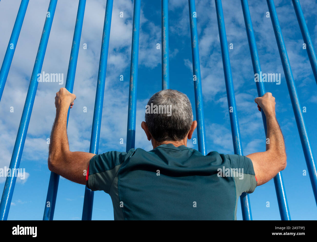 Rear, low angle view of man looking through steel bars. Depression, mental health, prison, asylum seeker, immigration... concept image. Stock Photo