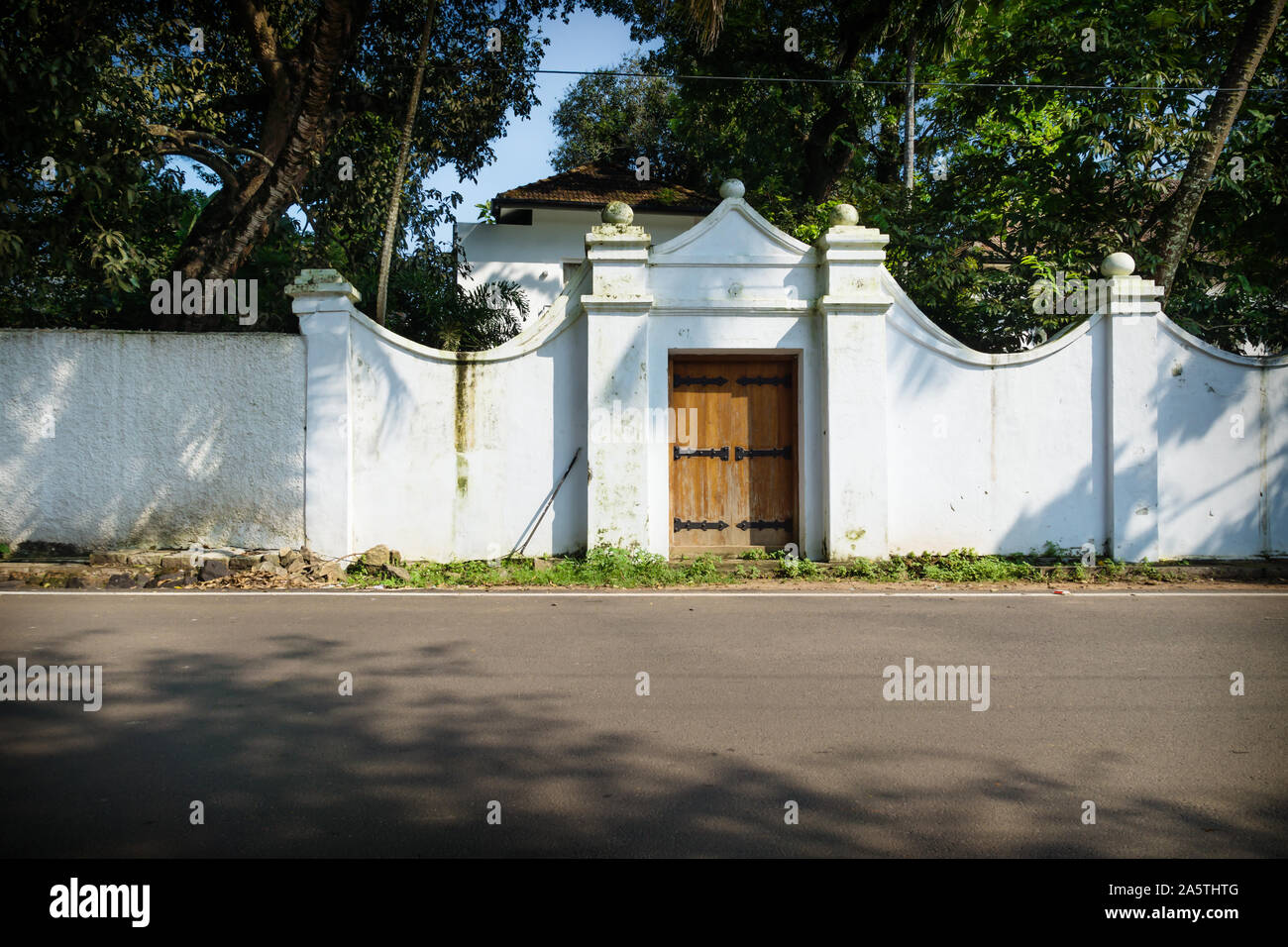 White colonial entrance of house along the road with green trees, Kochi, Kerala, India Stock Photo