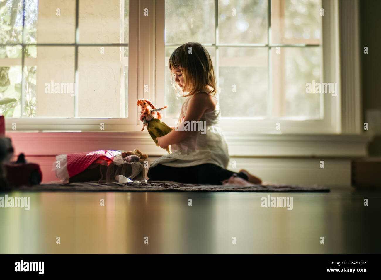 young girl playing dolls by window Stock Photo