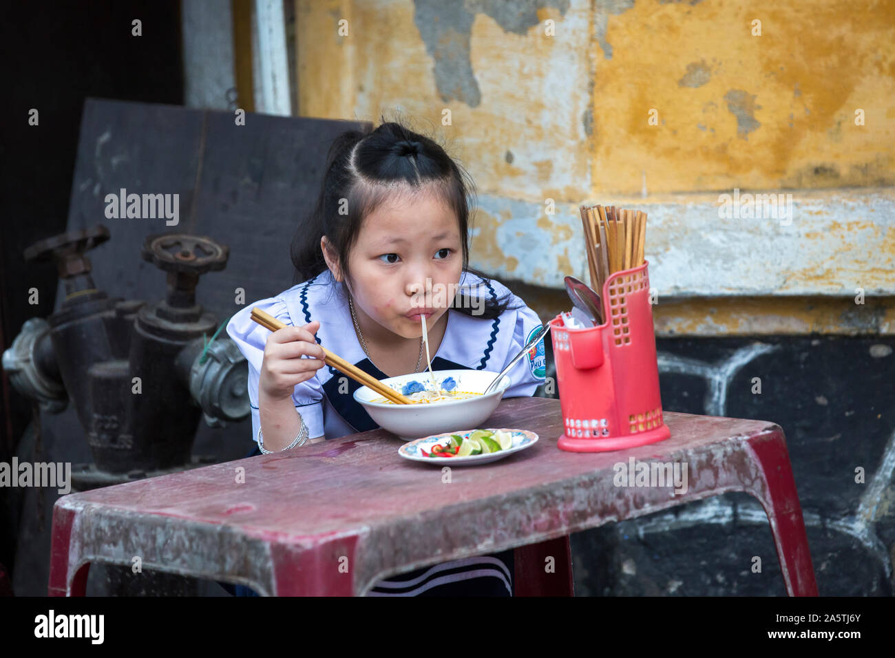 A young Vietnamese girl sucks up asian noodles. Stock Photo