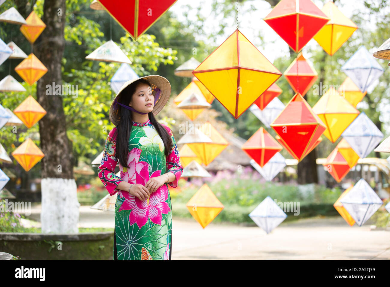 A young Vietnamese in traditional hat is surrounded by lanterns. Stock Photo