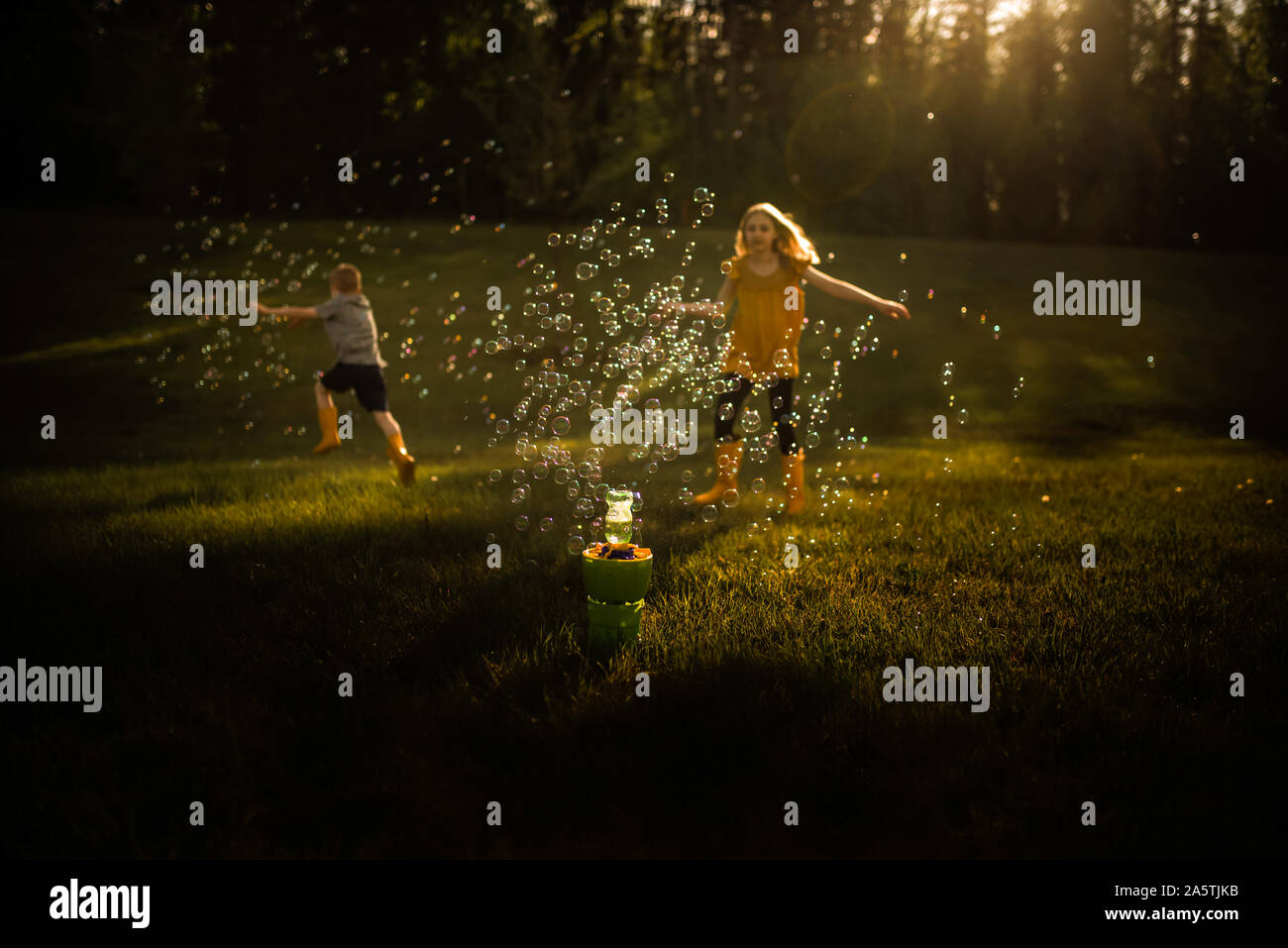 Siblings running through bubbles in golden light Stock Photo