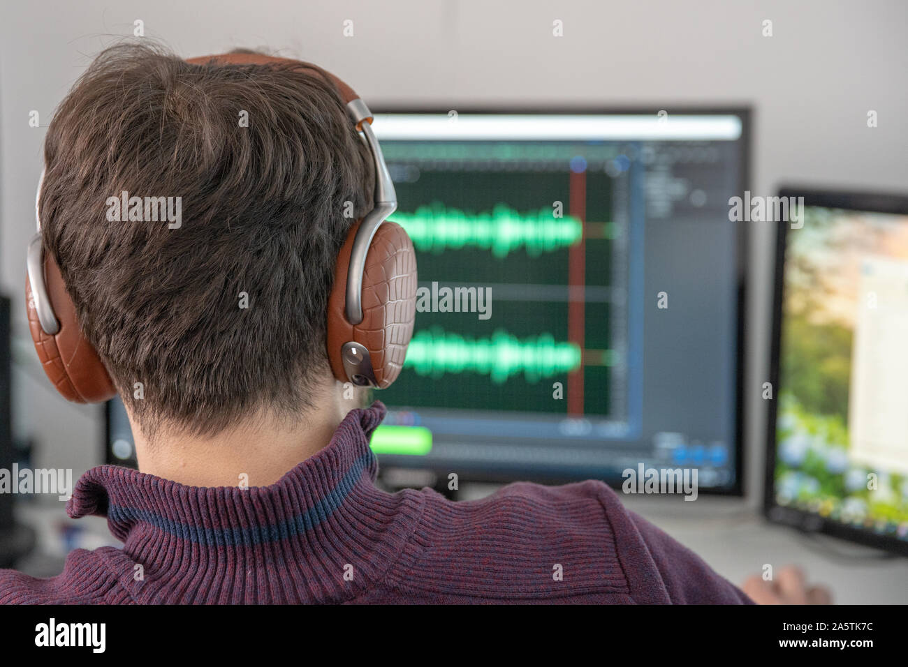 The man in the photo studio records and modifies singing, voice and music for commercial use. Works in an audio editor in a computer with headphone on Stock Photo