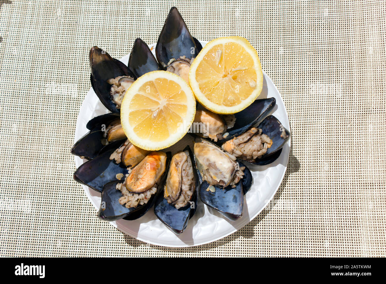 Top view of a plateful stuffed mussels accompanied by two halves of a juicy yellow lemon on a sunny day. Stock Photo