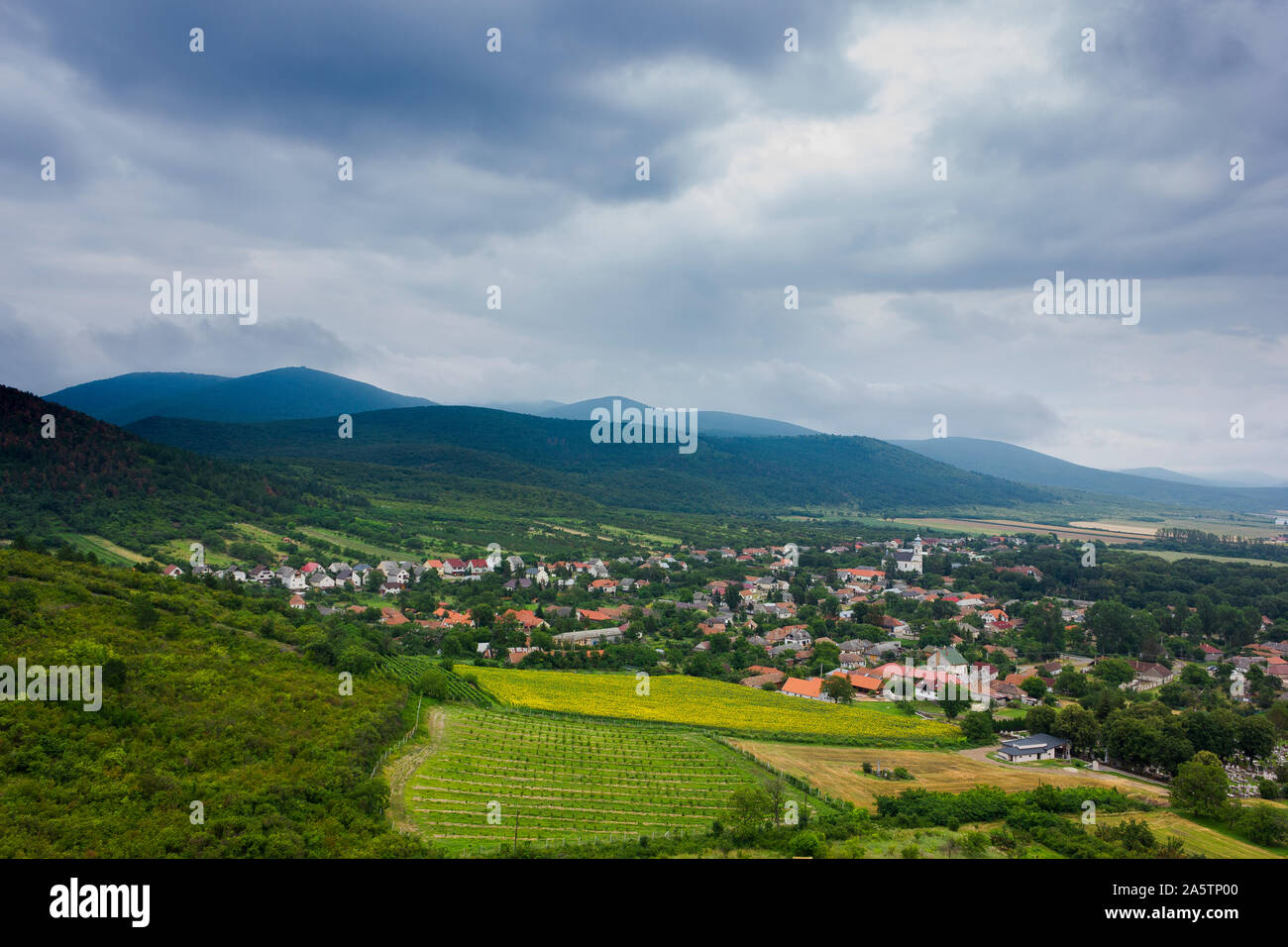 Small village in a valley. Hills, mountains and fields around. Summer day. Picture taken from the side of the hill. Stock Photo