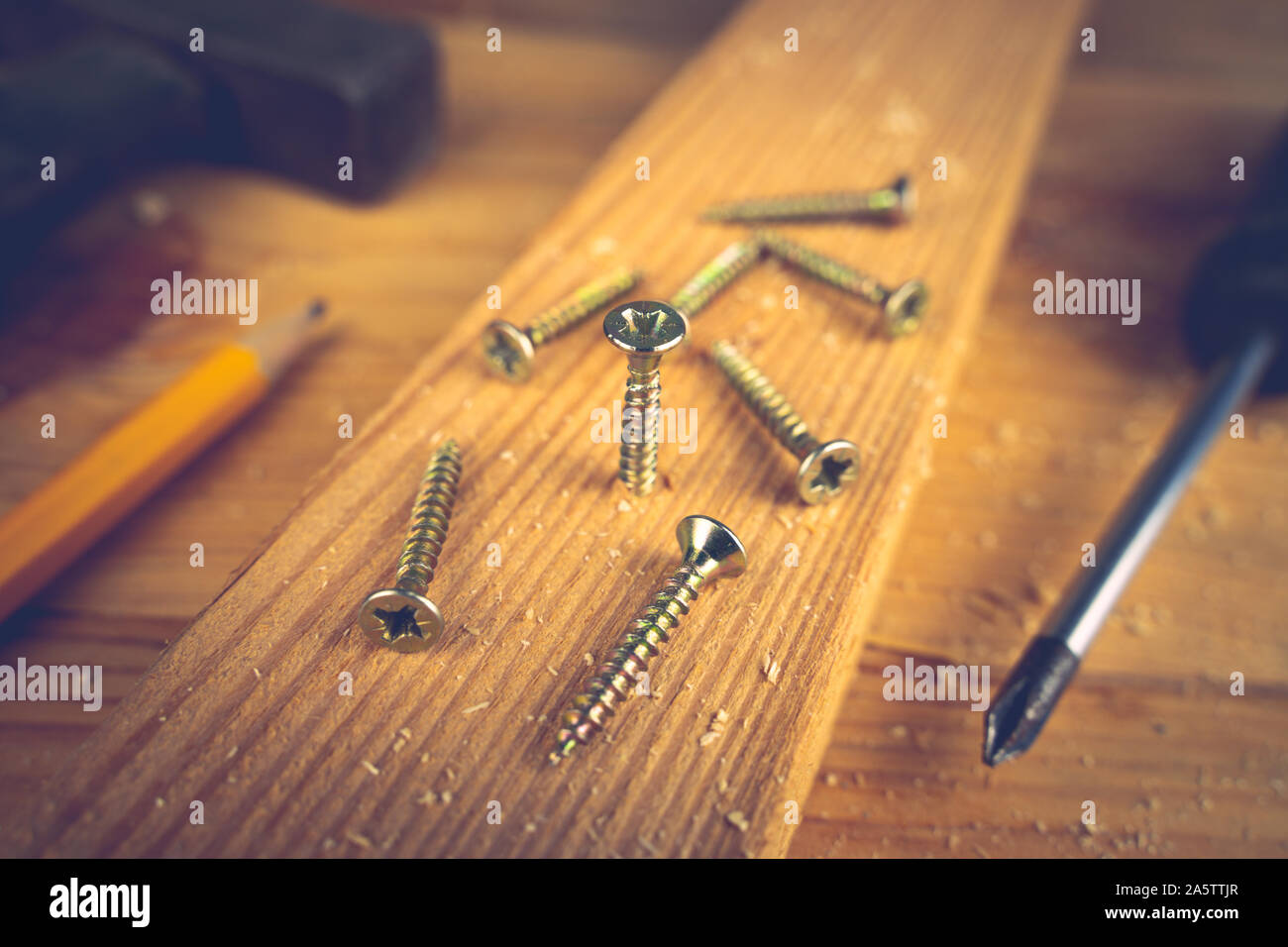 Screws, screwdriver, hammer and a pencil on a wood table. Concept tools and repair work. Stock Photo